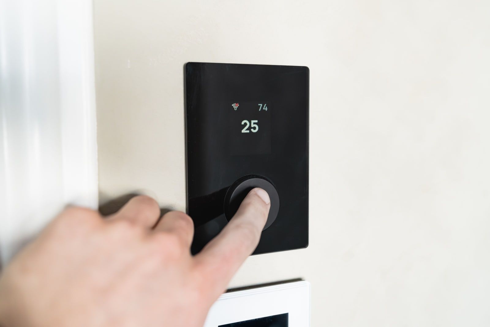 A finger pressing the dial of a smart thermostat on a wall