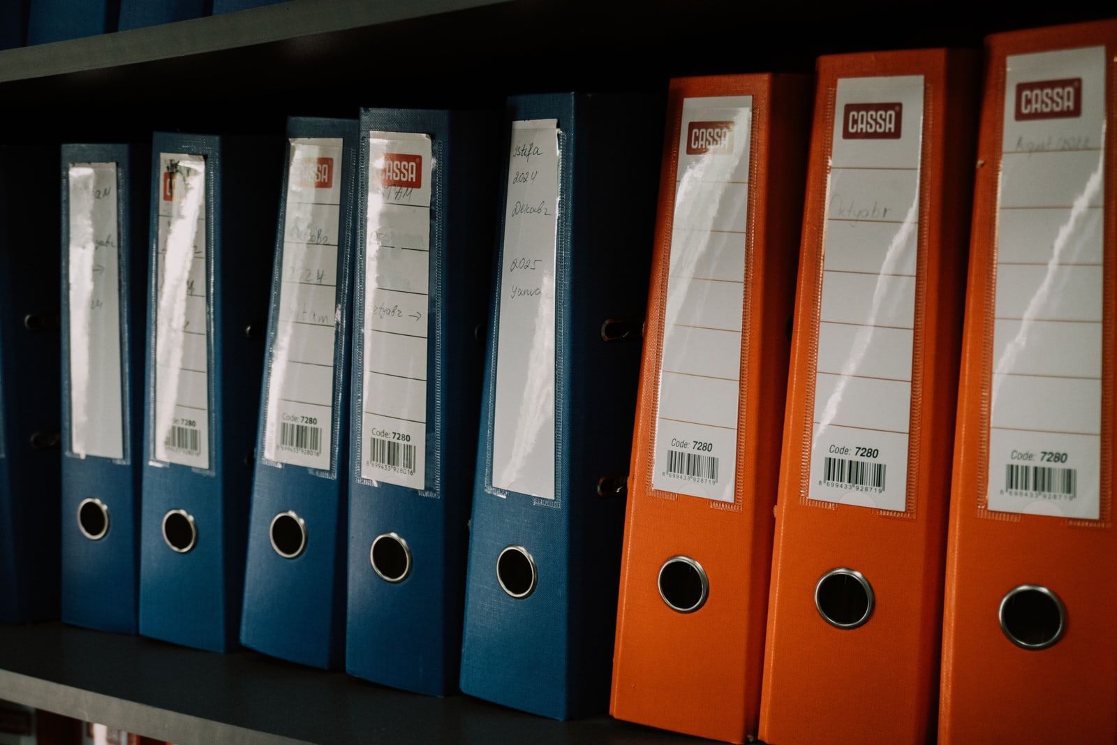 A row of blue and orange ring binders standing on an office shelf