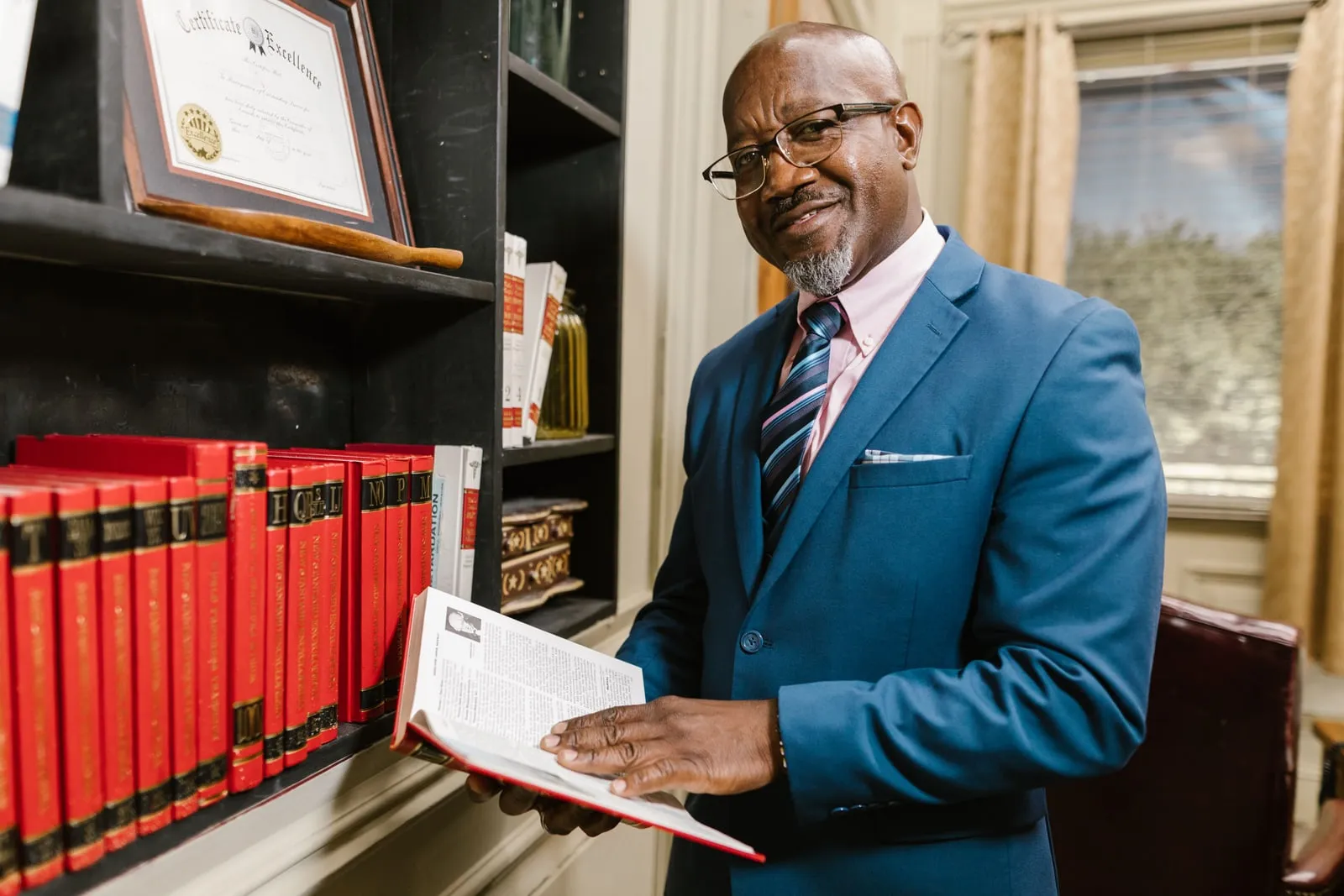 A person holding an open law book beside a shelf of legal volumes