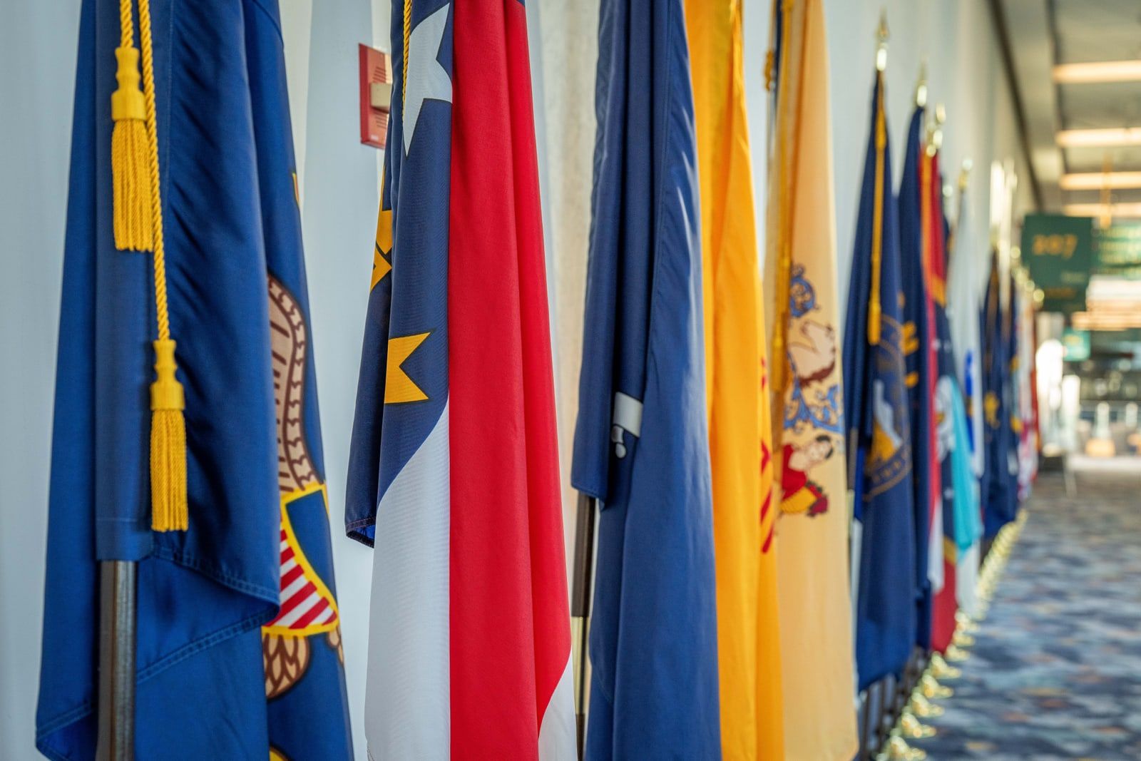 A row of flags on poles along an indoor corridor