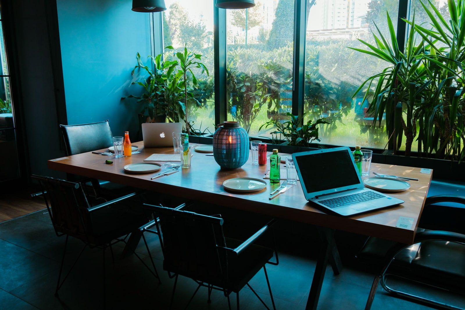 Two laptops open on a long table beside a window