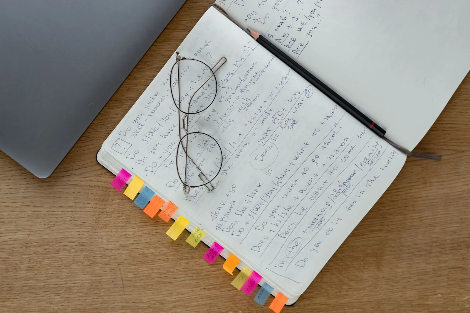 An open notebook of handwritten notes with reading glasses and a pencil