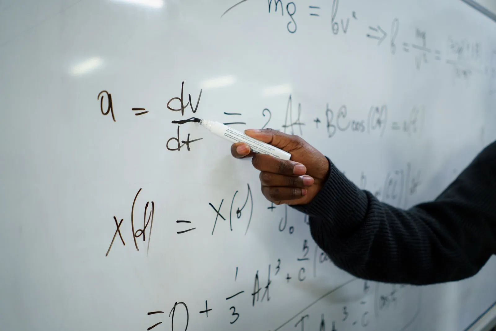 A hand writing mathematical equations on a whiteboard