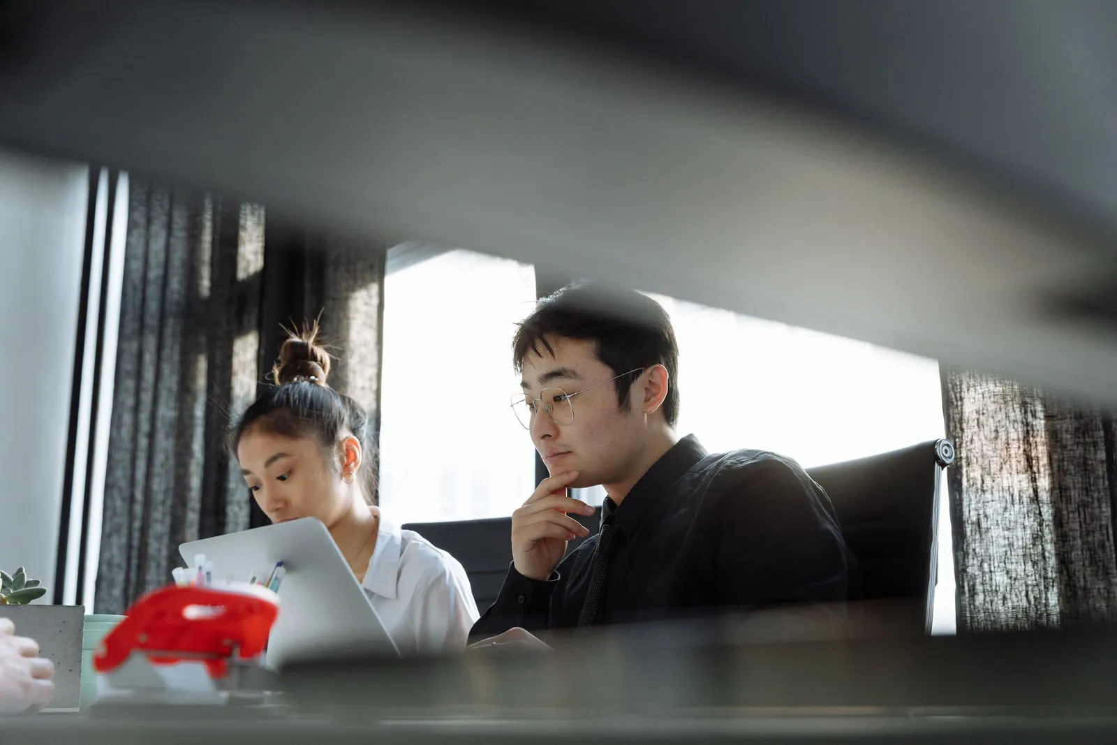 Two colleagues working side by side at a desk with a laptop