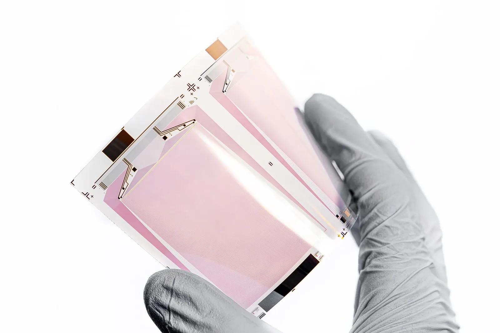 A gloved hand holding a thin semiconductor substrate up to the light