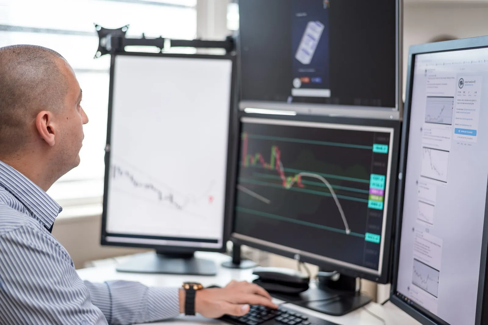 A person at a desk watching trading screens filled with candlestick charts