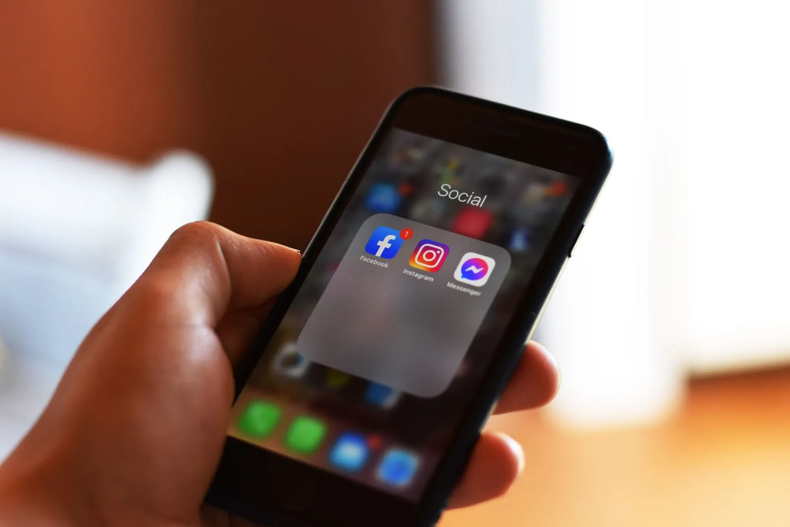A hand holding a smartphone showing a grid of apps