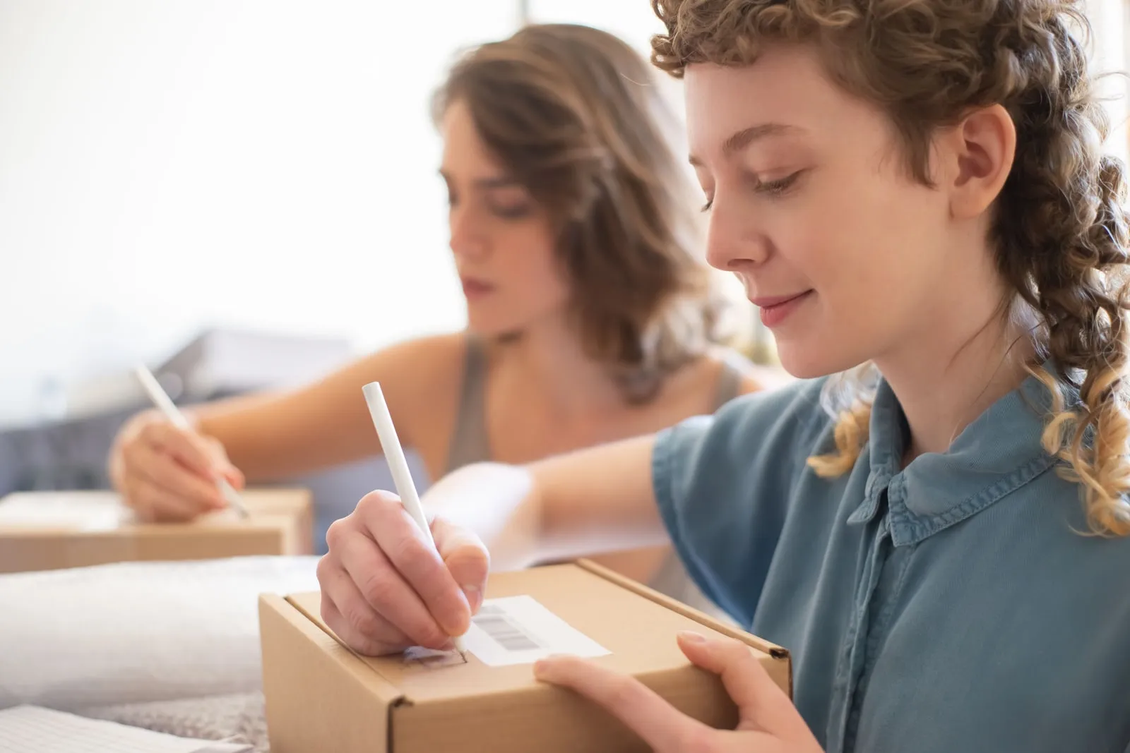 Two people labelling cardboard parcels at a table