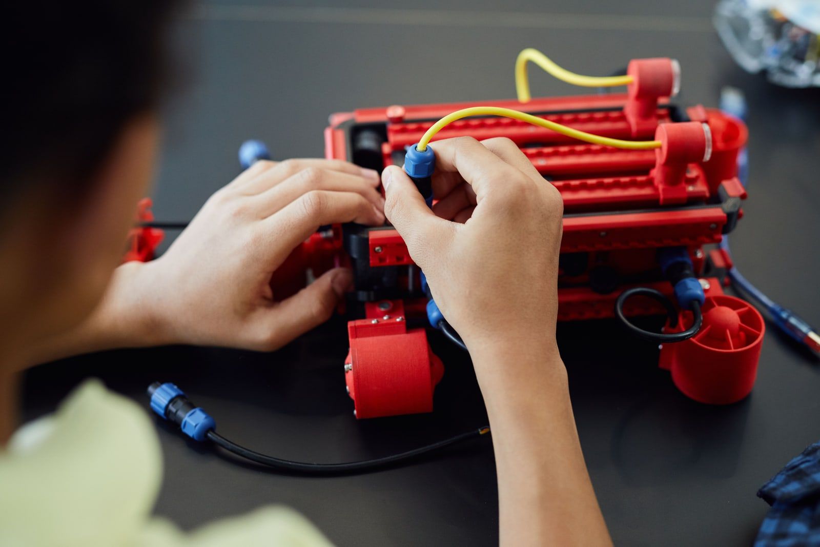 A person assembling a red educational robot kit with cables on a dark bench