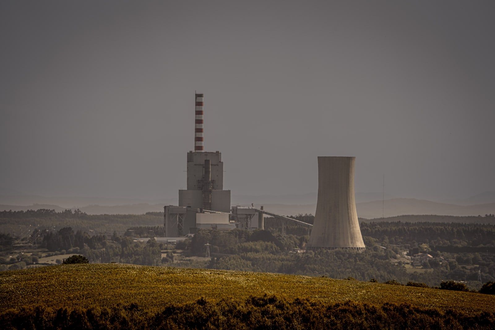 A power station with a striped chimney and a cooling tower beyond a field