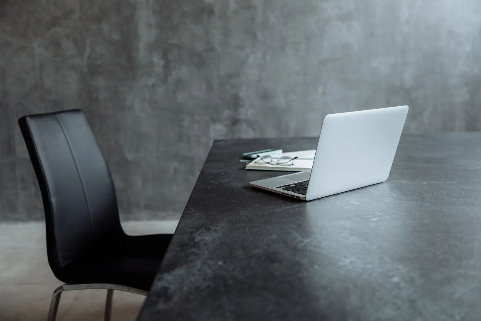 Laptop and glasses on an empty desk beside a chair