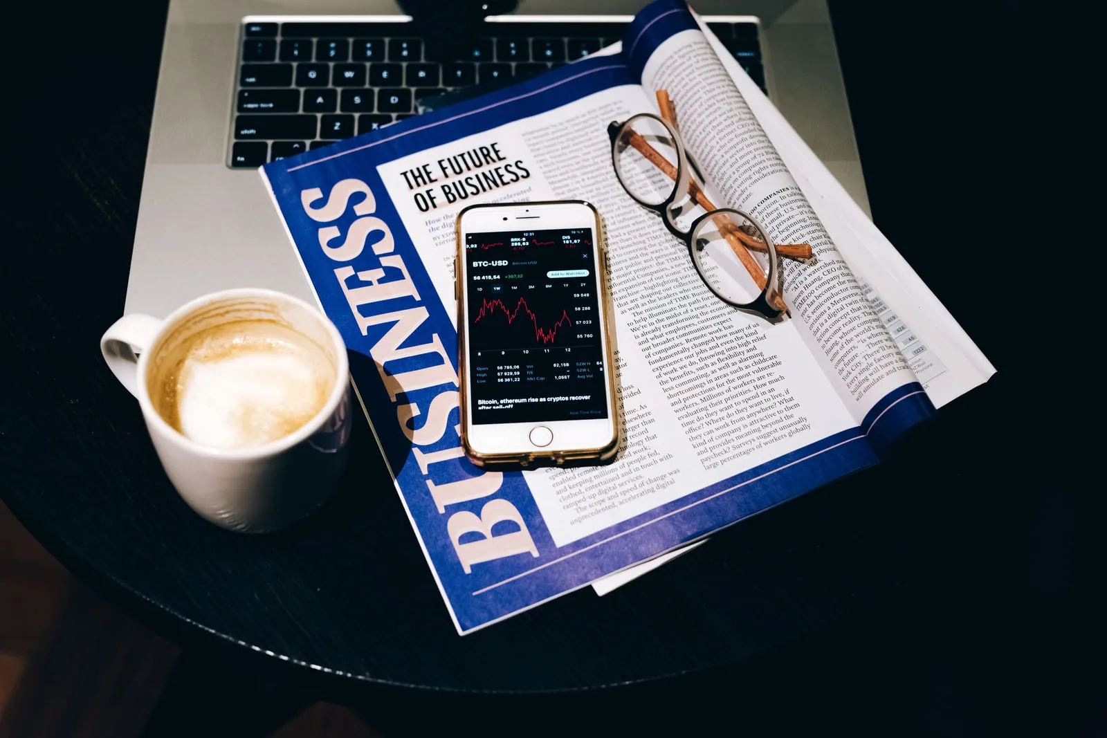 A business magazine open on a table beside a phone showing a price chart