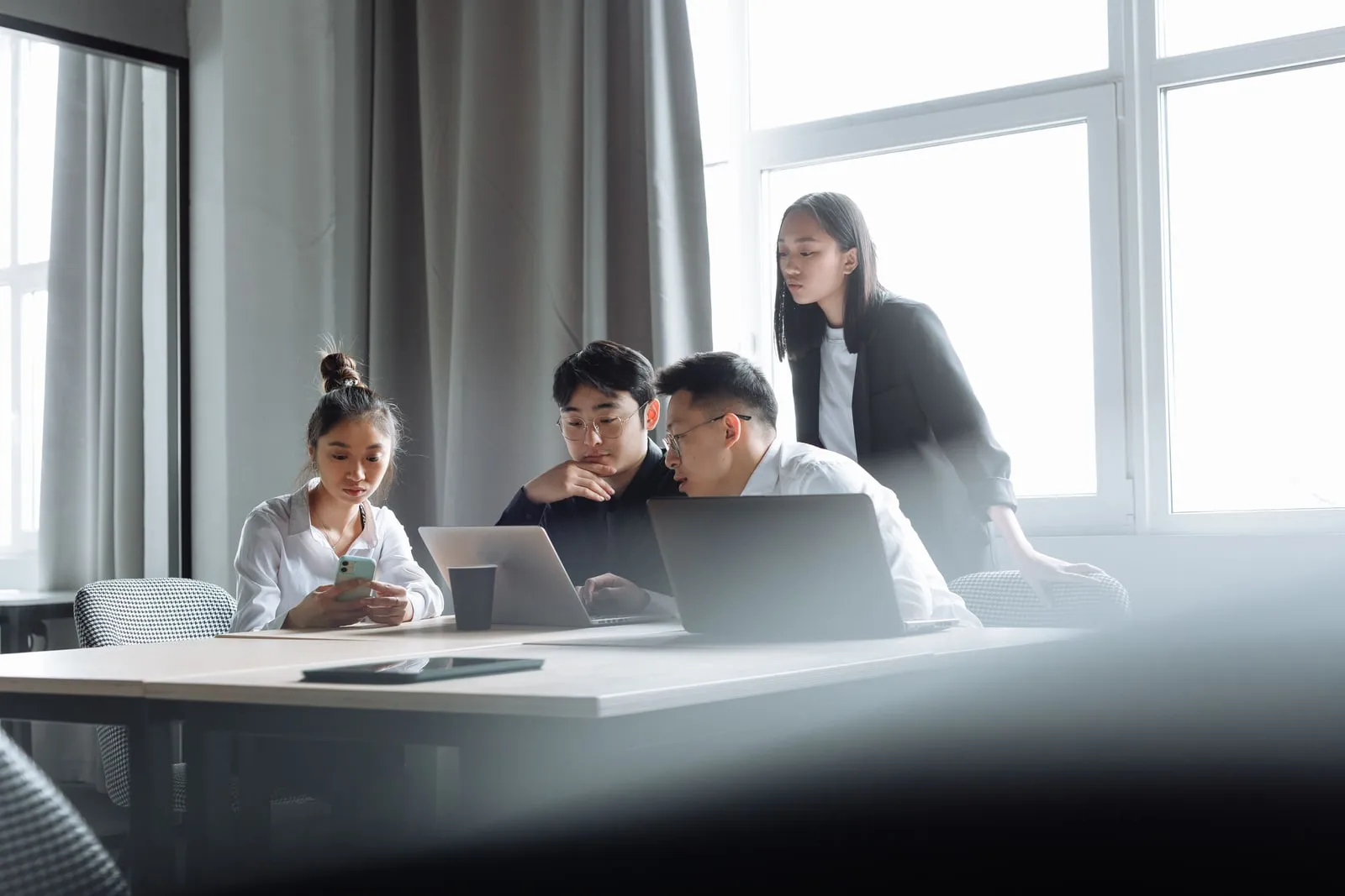 Colleagues in a meeting room gathered around an open laptop