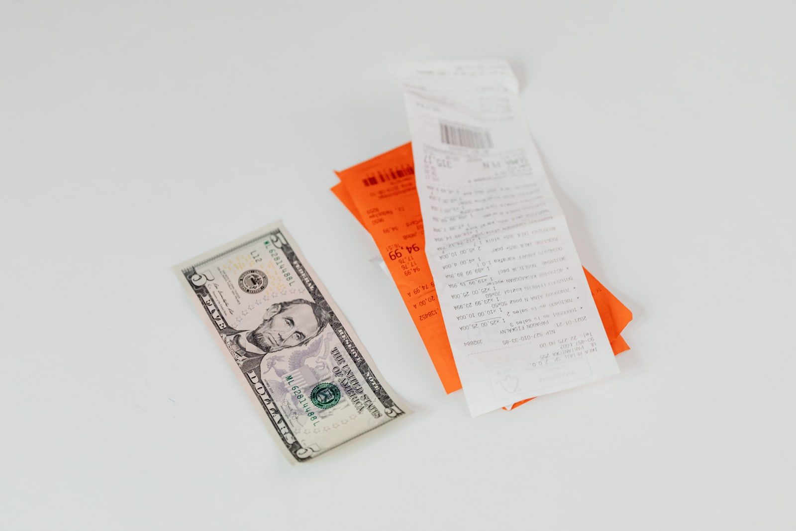 Two paper receipts and a five-dollar note on a white surface