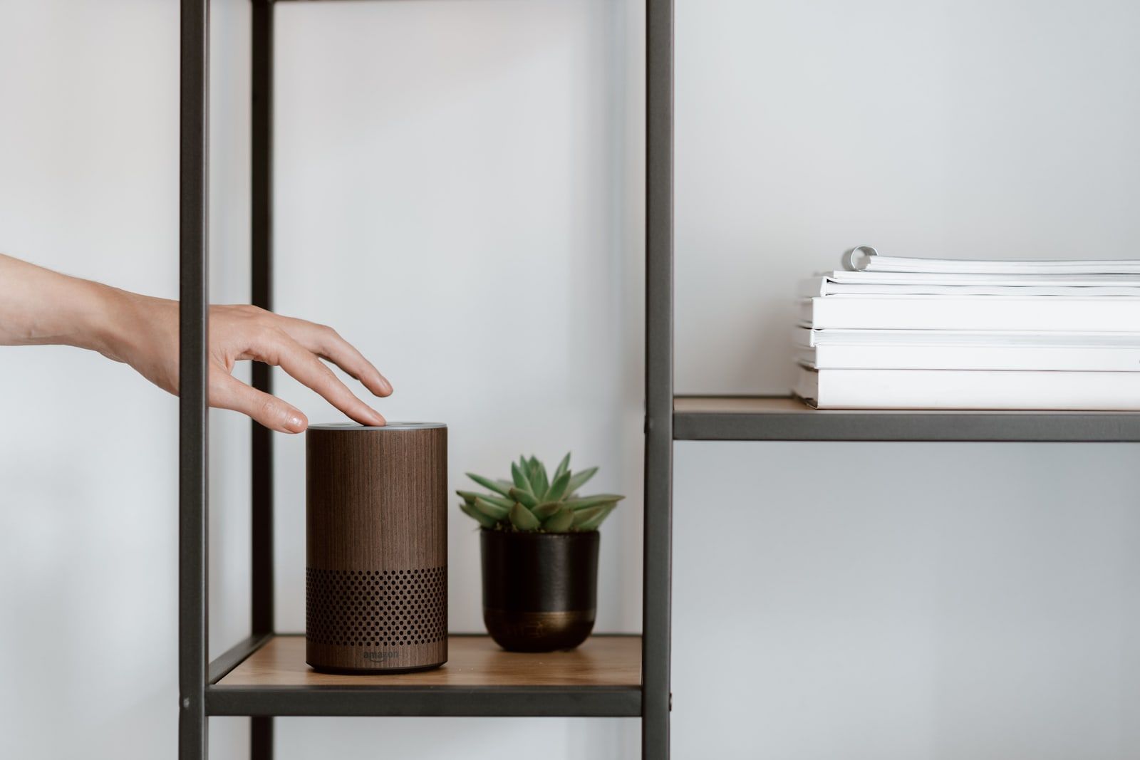 A hand reaching for a smart speaker on a shelf
