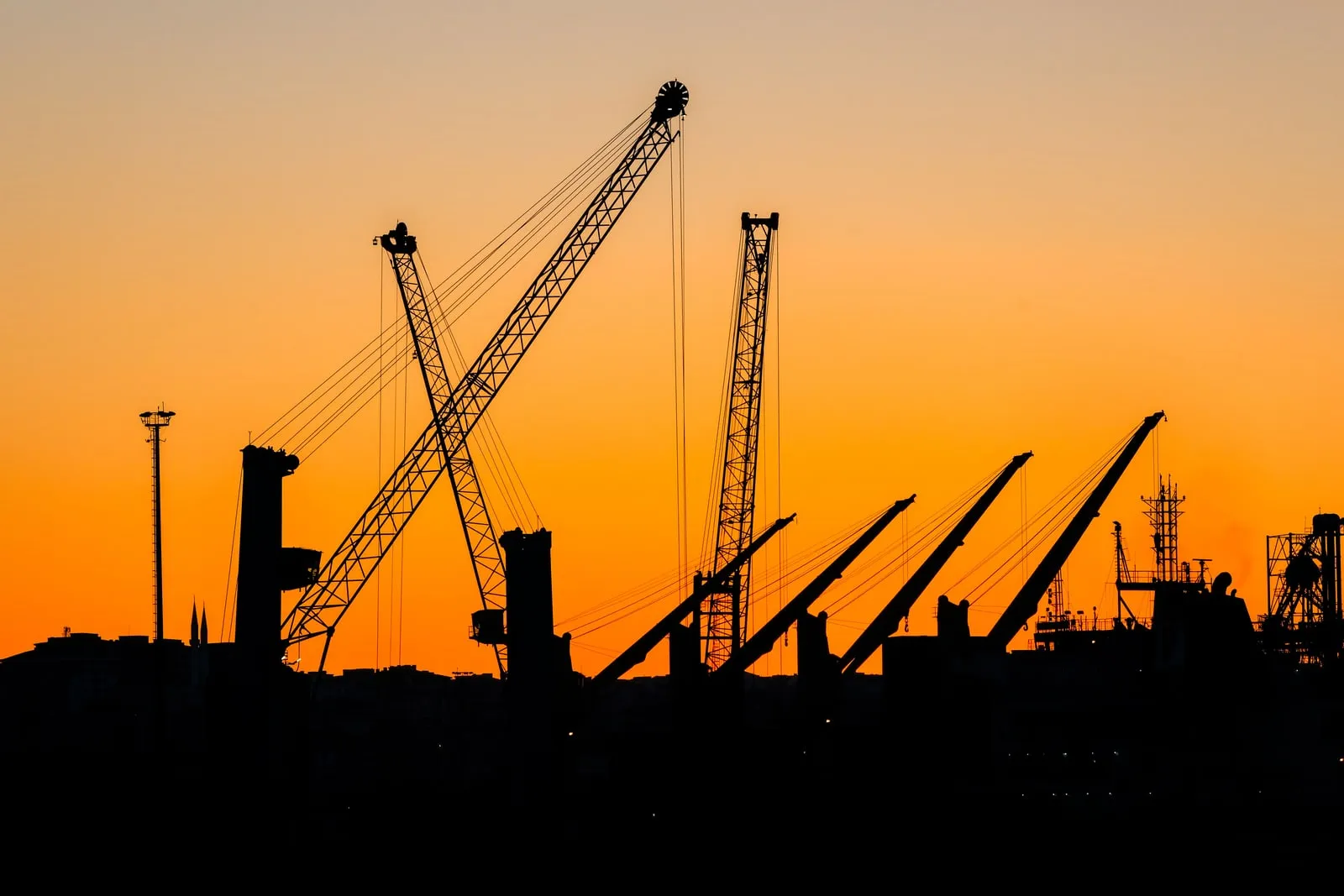 The silhouettes of harbour cranes against an orange sunset sky