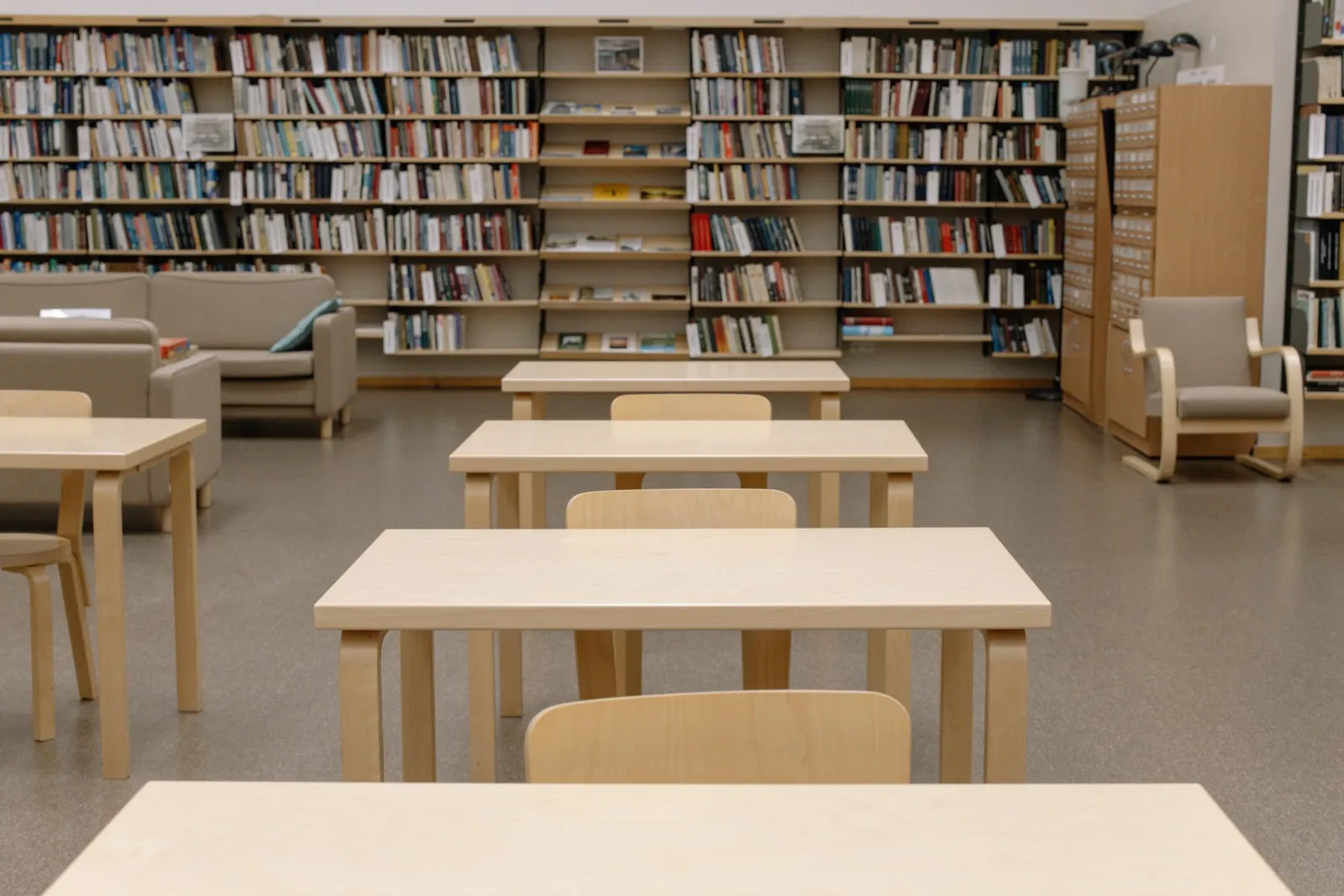 Uma sala de leitura de biblioteca com mesas de madeira clara e estantes de livros