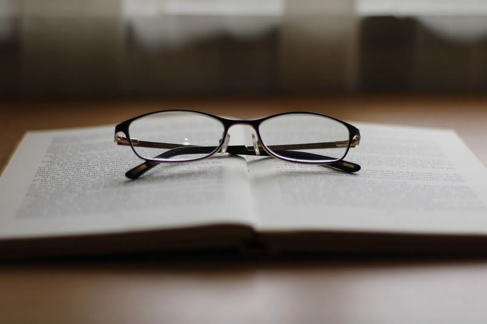 An open book on a desk beside a pair of reading glasses