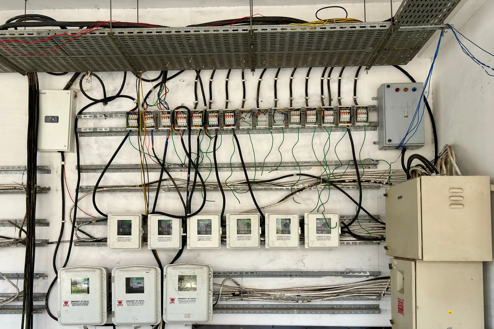 A wall of electricity meters and circuit breakers with cable trays above