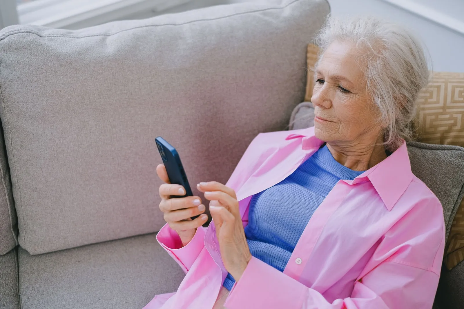 An older woman sitting on a sofa using a smartphone