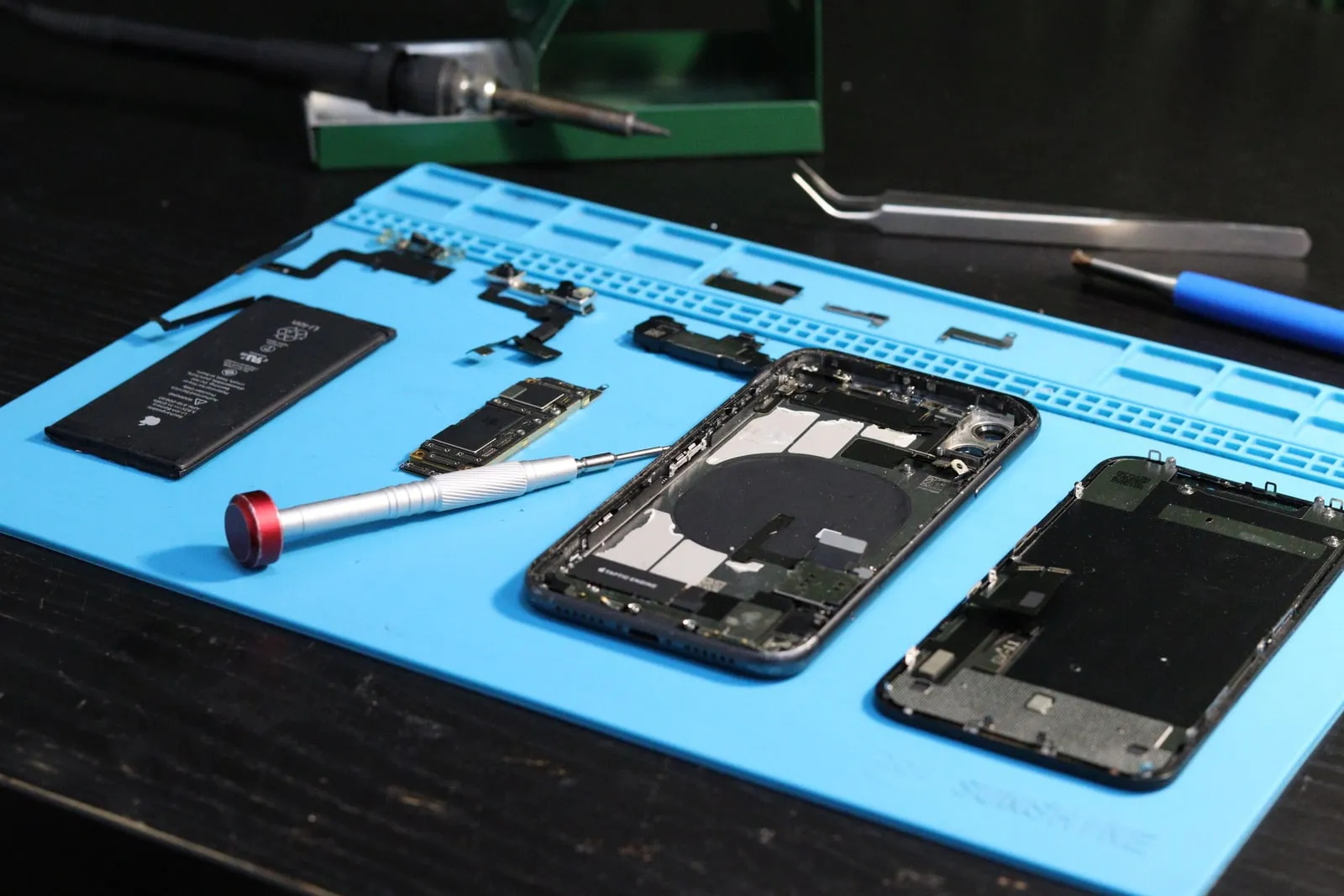 Disassembled smartphone parts and tools on a repair mat