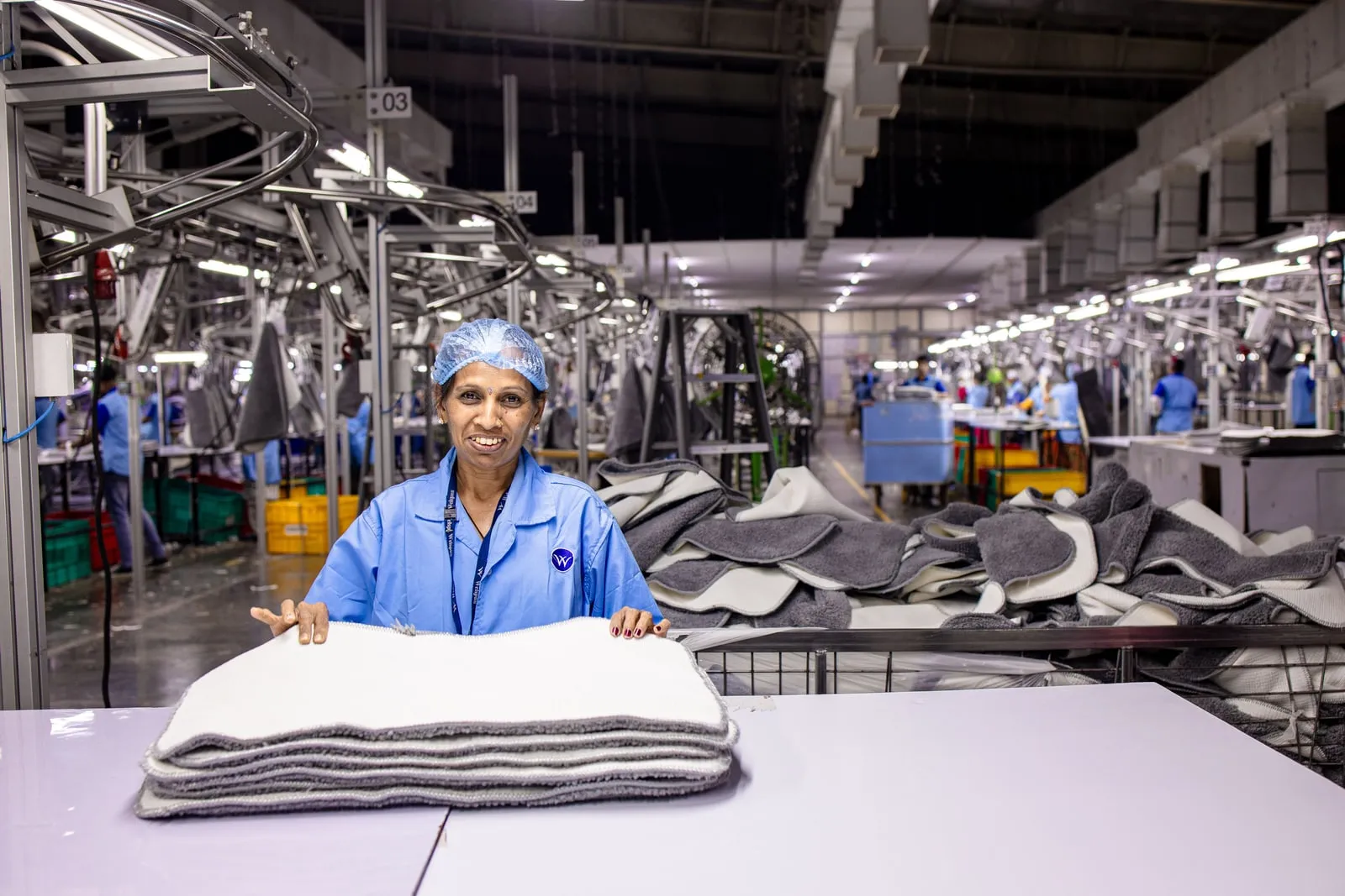A worker folding textiles at a bench on a factory production line