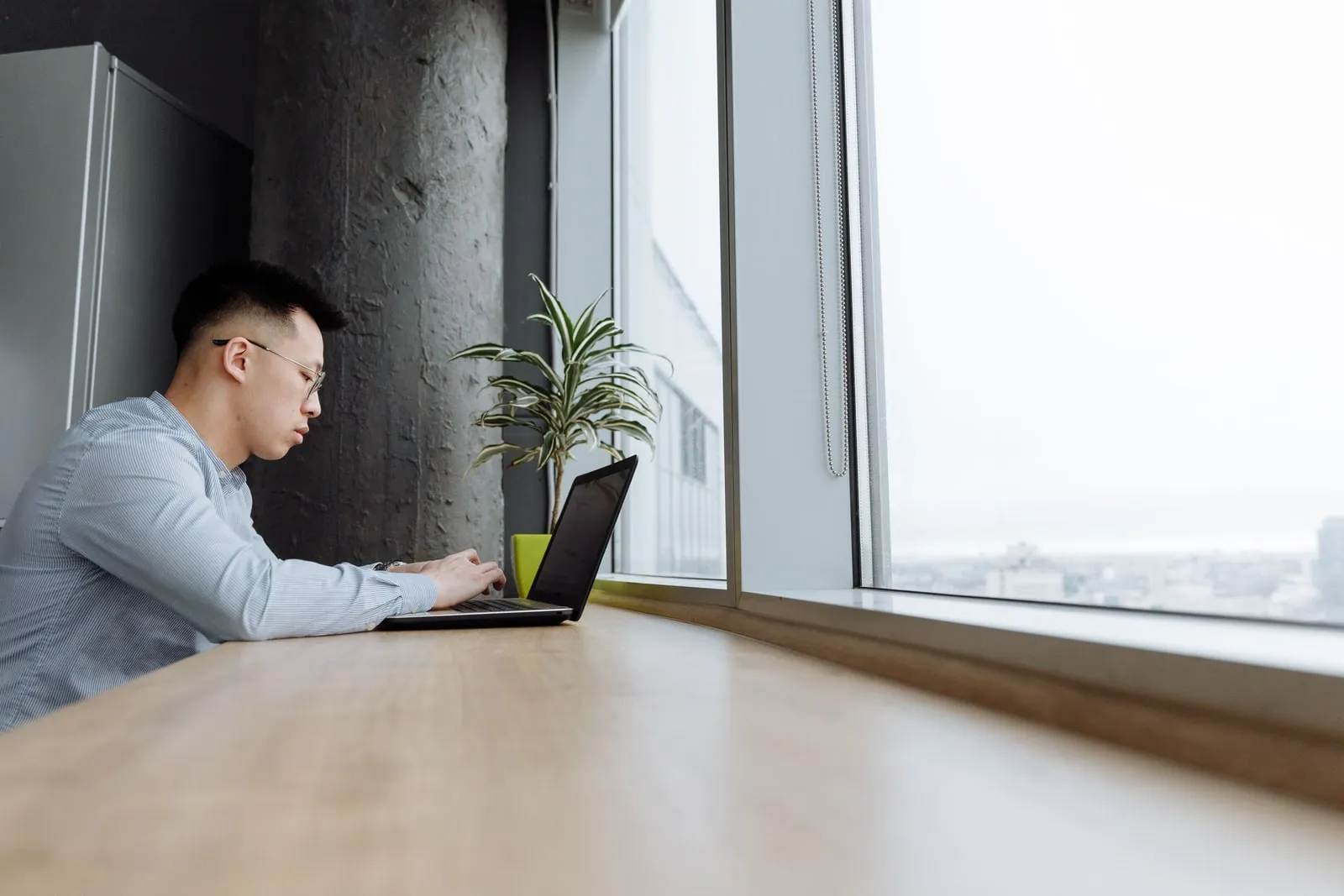 A person working on a laptop at an office desk by a window