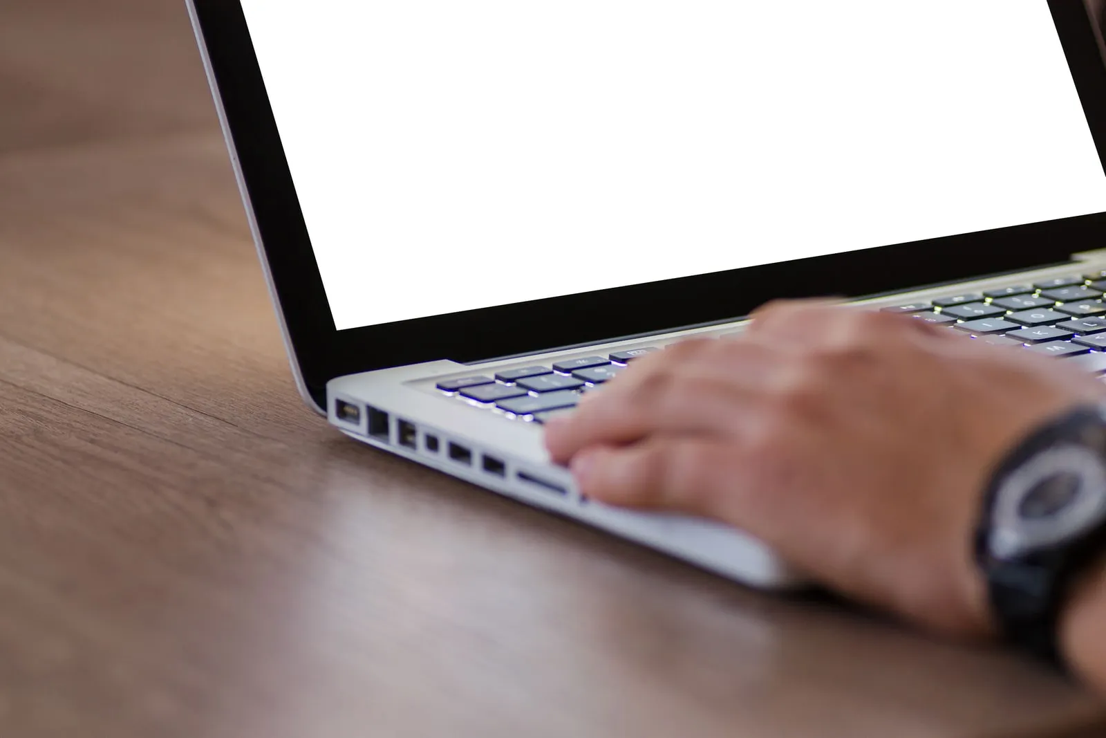 Hands typing on a laptop keyboard at a wooden desk