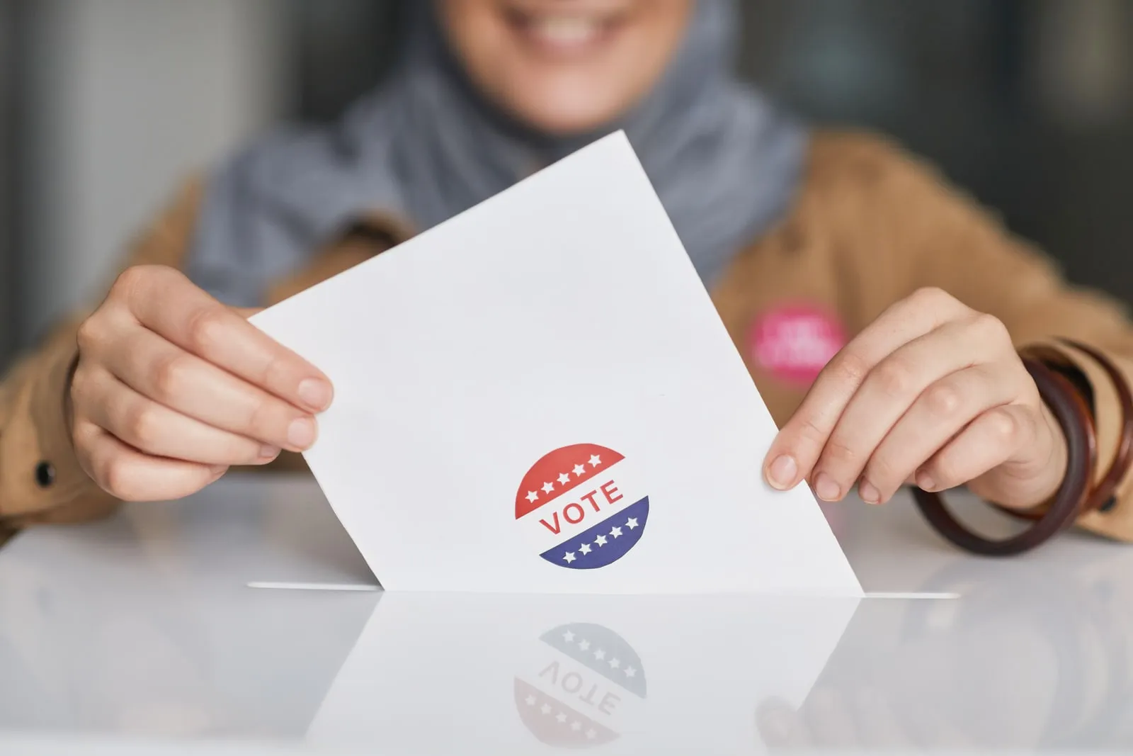 A hand dropping a folded paper into a ballot box