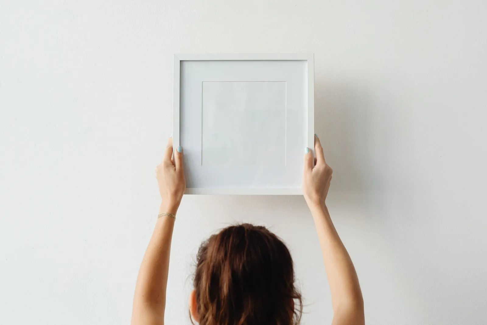 A person hanging an empty picture frame on a wall