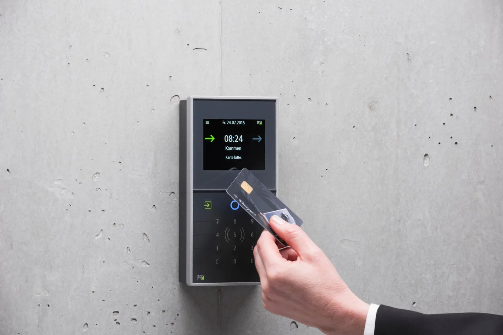 A hand holding an access card up to a wall-mounted card reader
