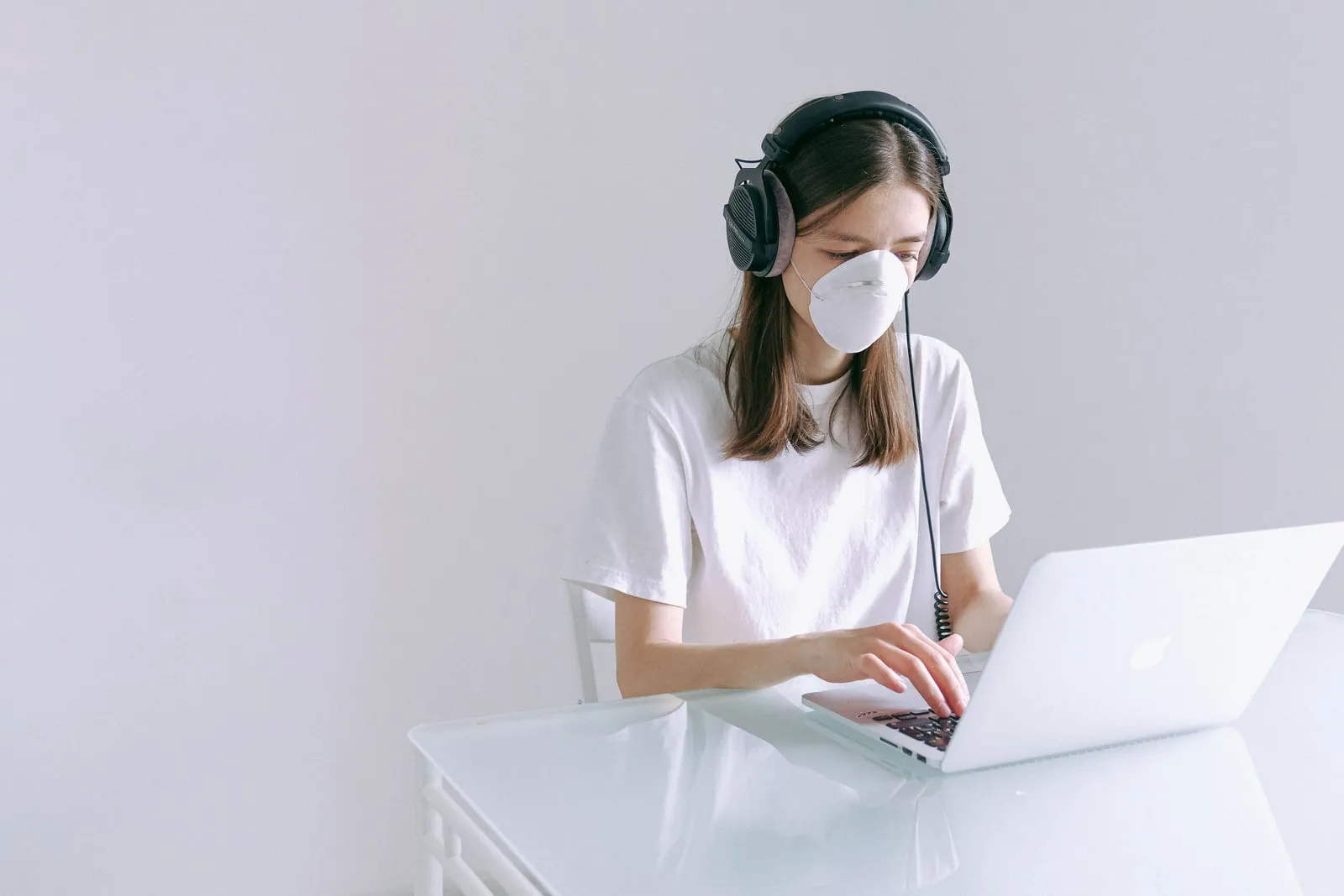 Person wearing headphones and a face mask typing on a laptop