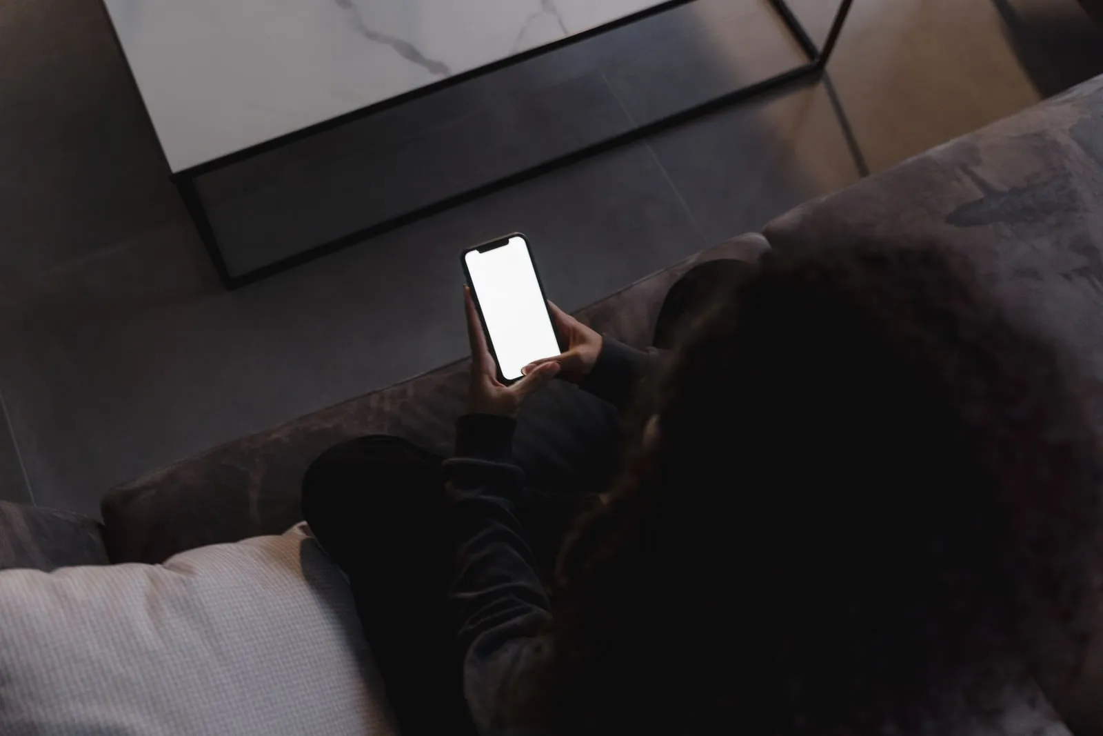 A person holding a smartphone in low light indoors
