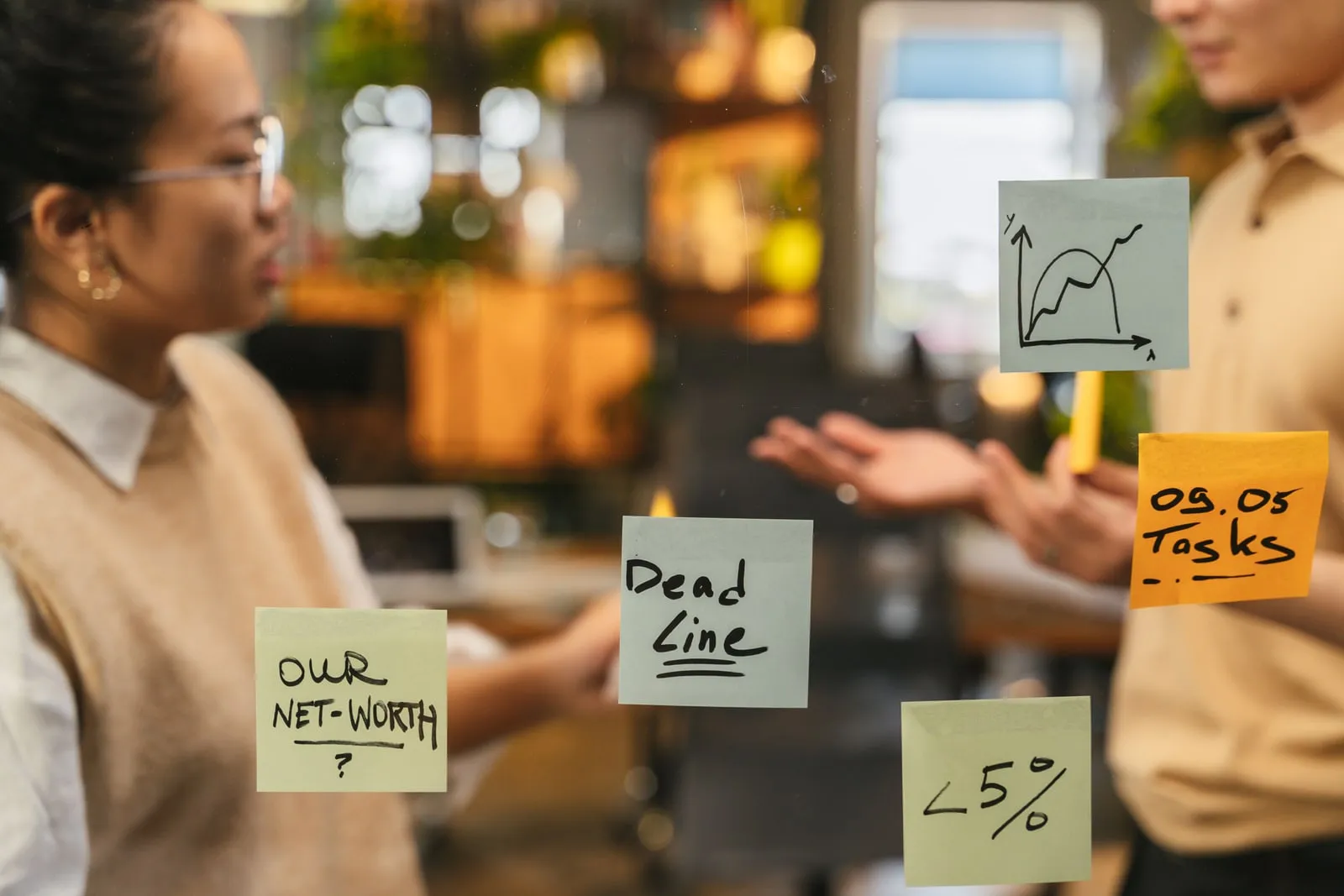 Sticky notes on a glass wall with two colleagues talking behind it