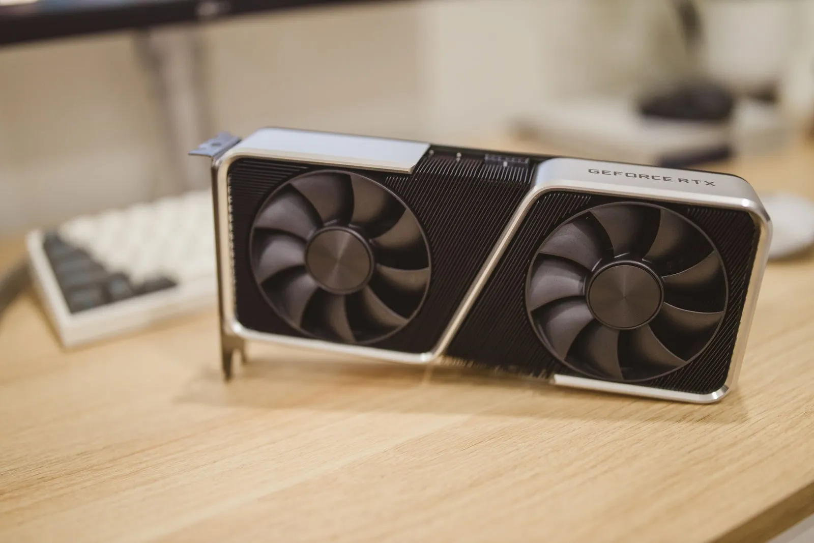 A graphics card lying on a wooden desk beside a keyboard