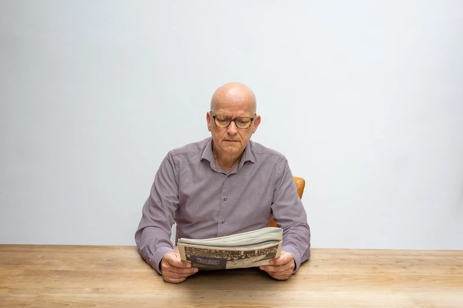 A person reading a printed newspaper at a table