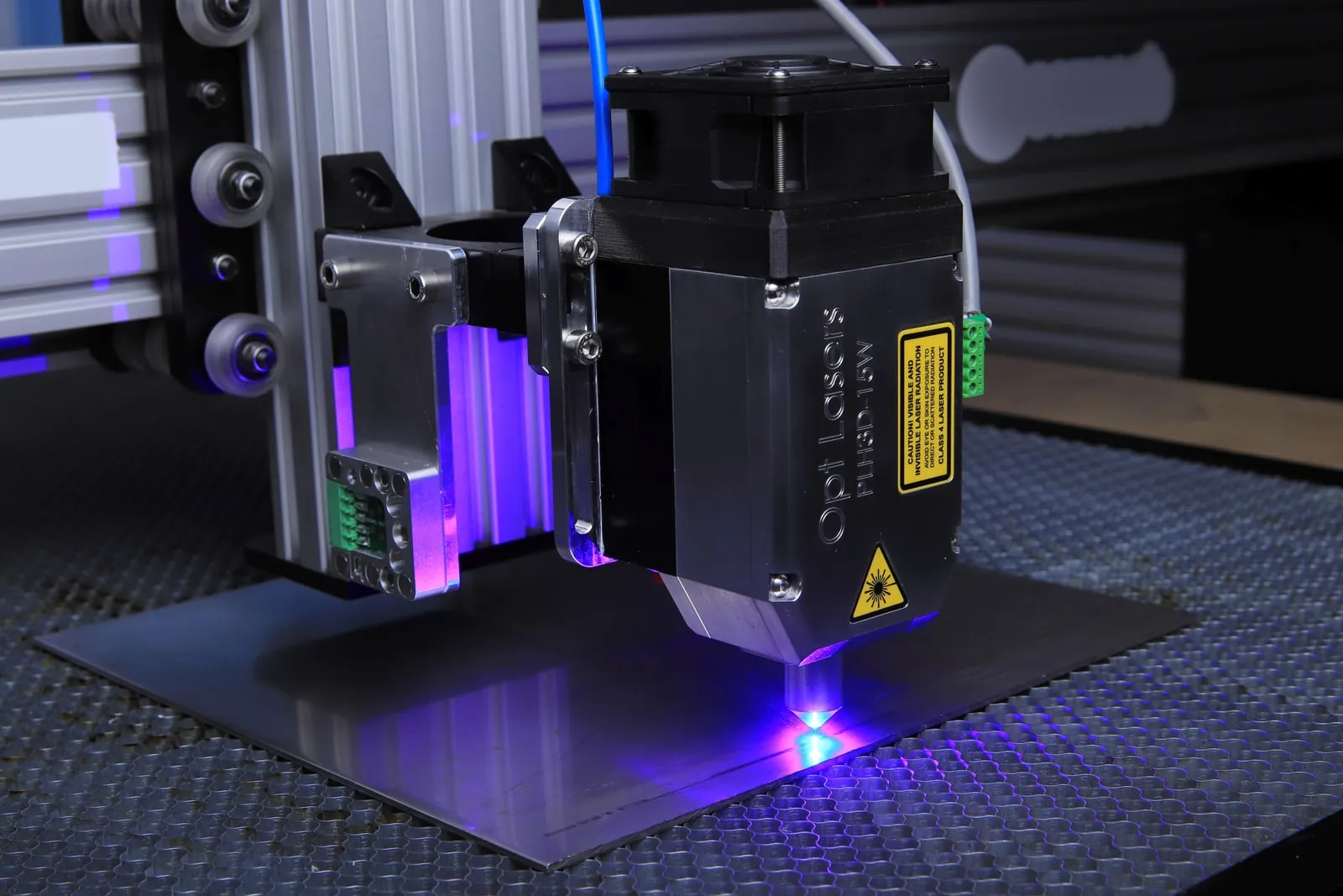 A blue laser head cutting into a metal sheet on a machine bed