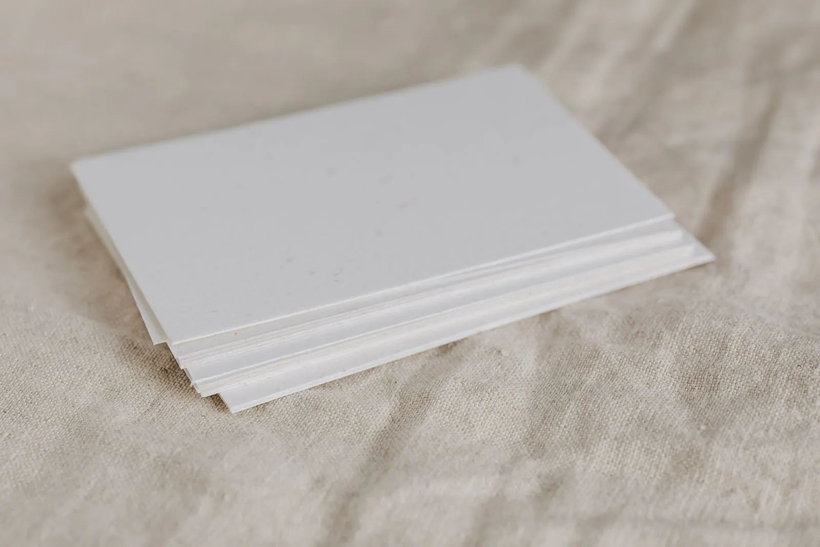 A small stack of blank white paper sheets on a linen cloth