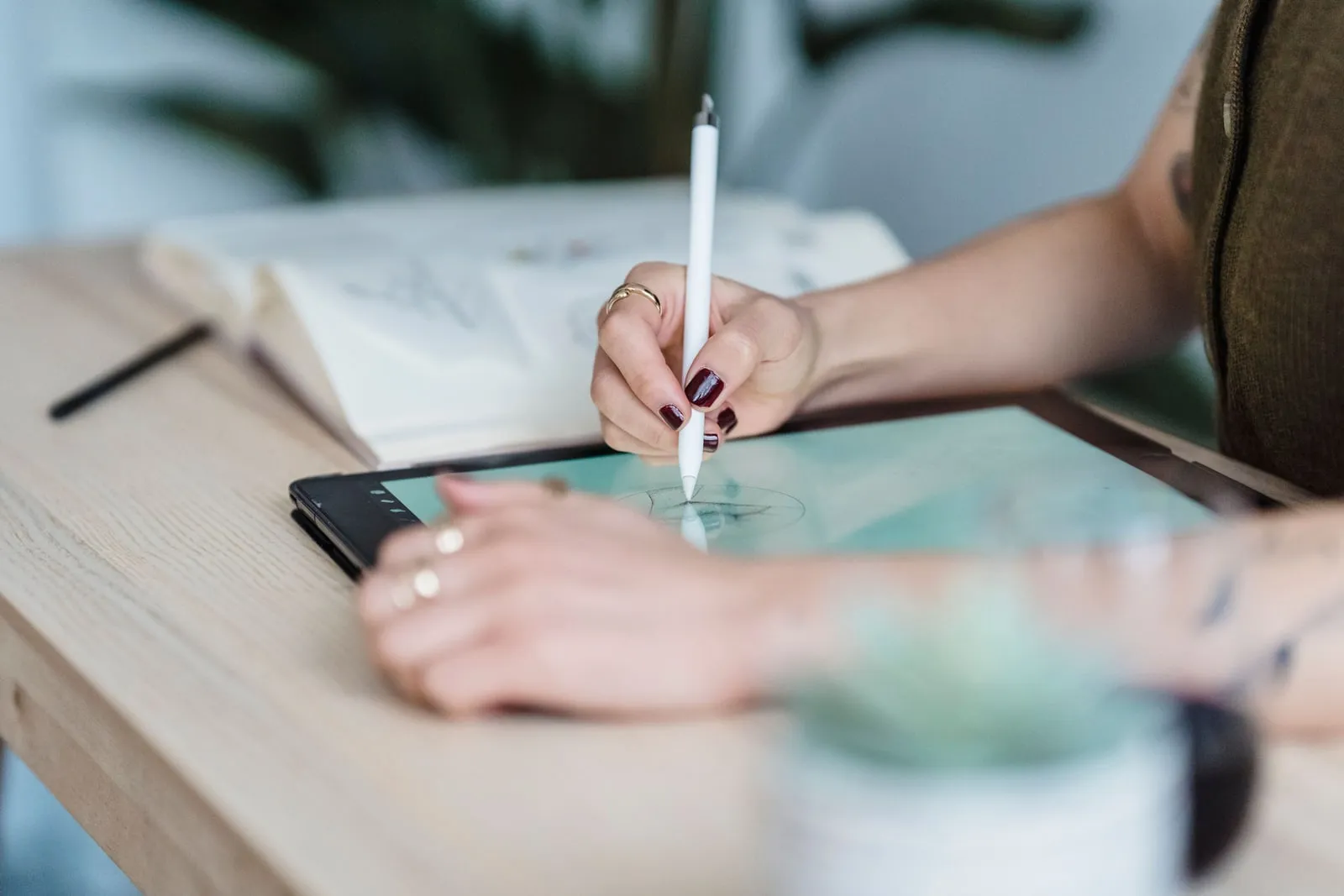 A designer sketching on a tablet with a stylus beside a notebook