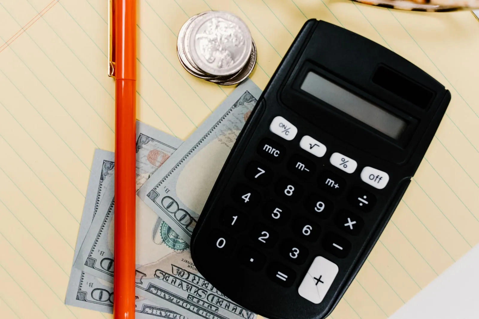 Une calculatrice, un stylo et des billets américains posés sur un bloc-notes