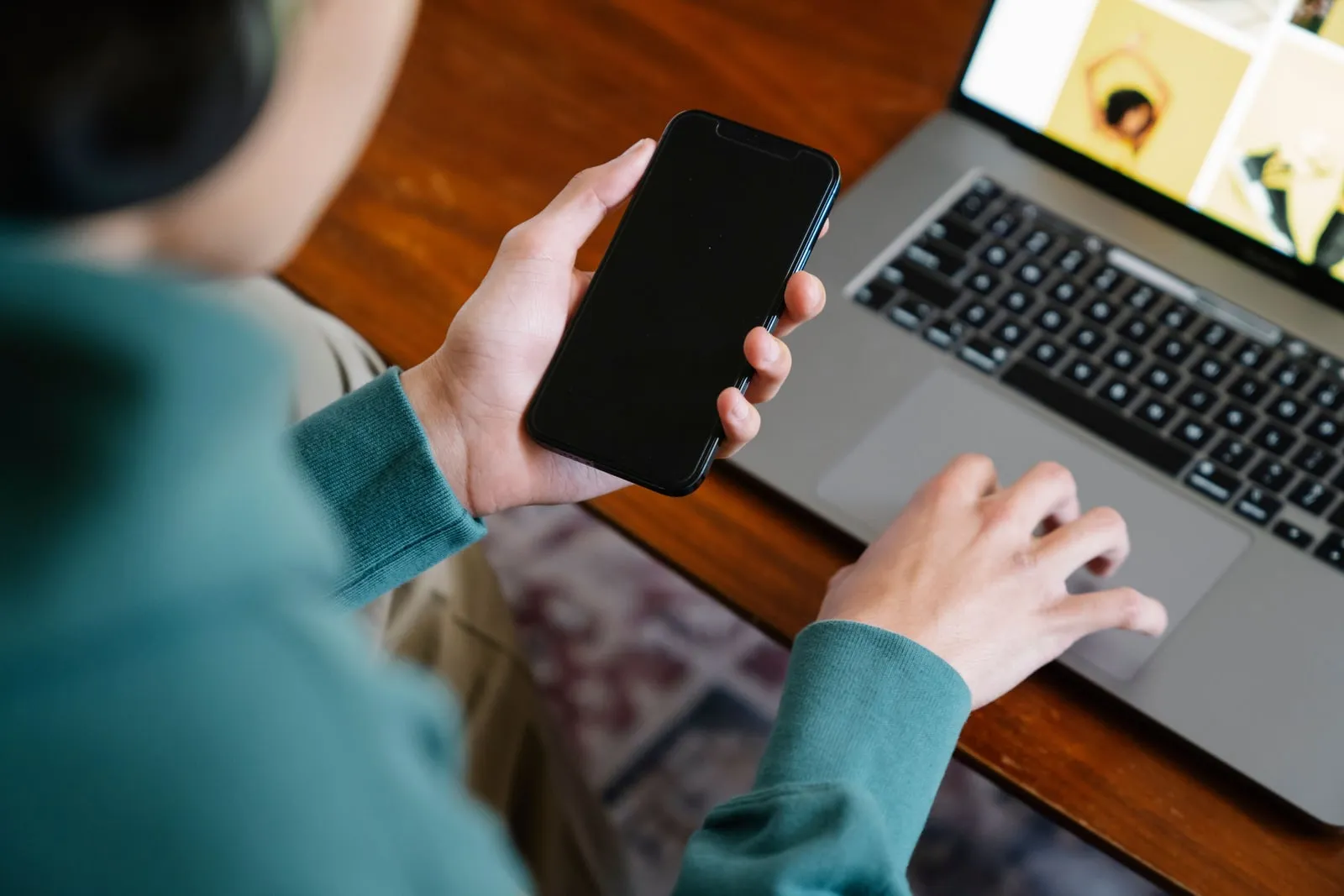 A person holding a smartphone next to a laptop