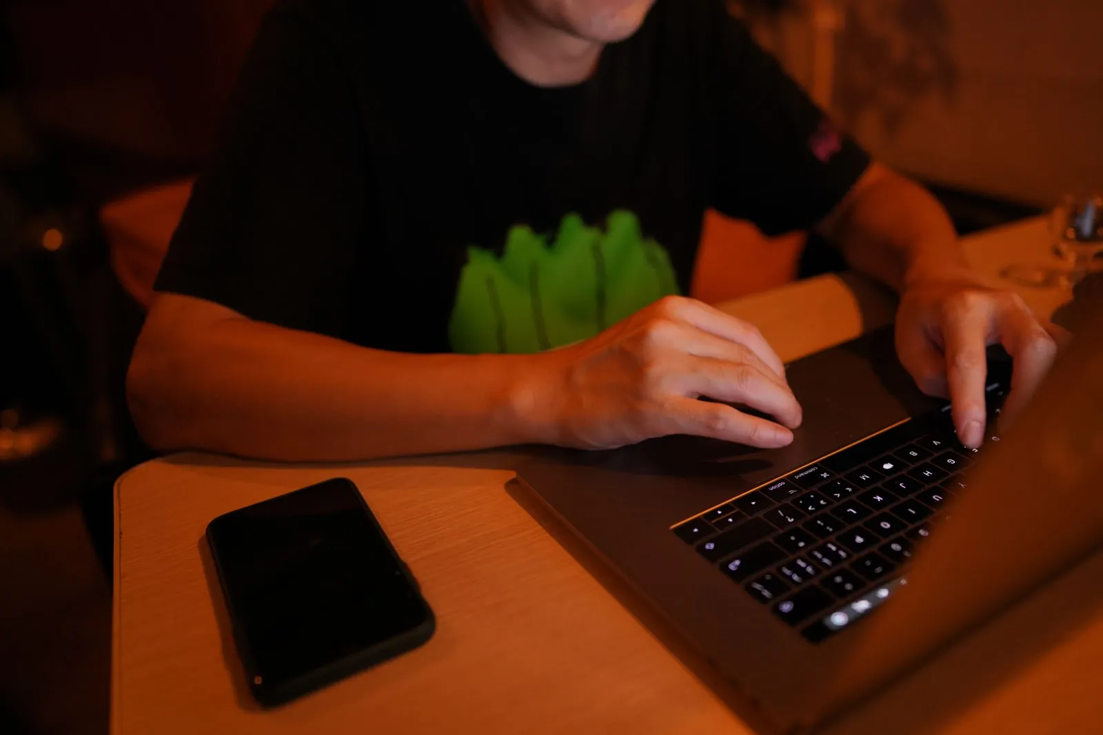 A person typing on a laptop at a desk at night