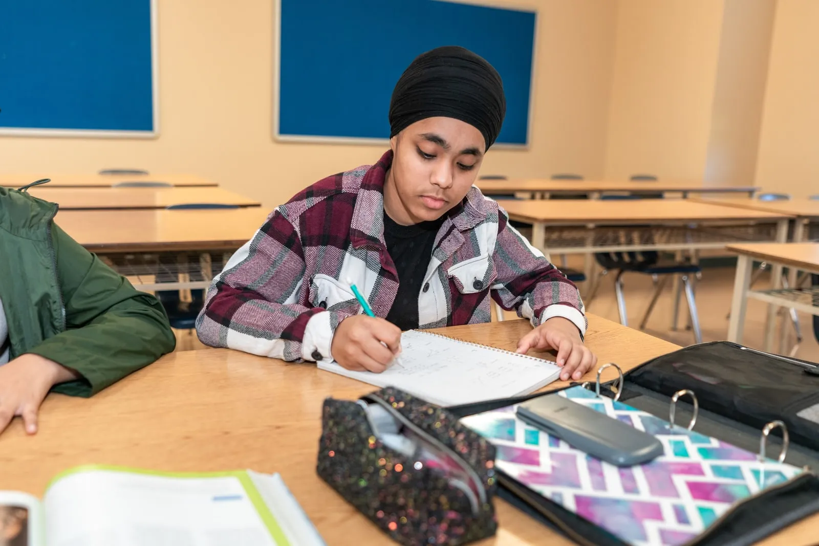 A student writing in a ring-bound notebook at a classroom desk