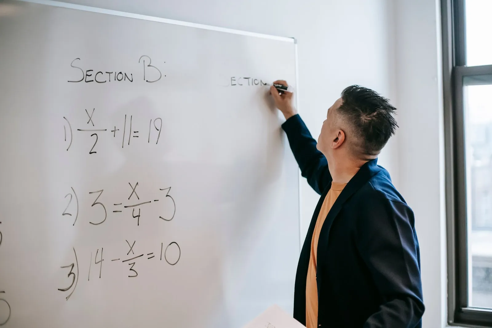 A man writing algebra equations on a whiteboard