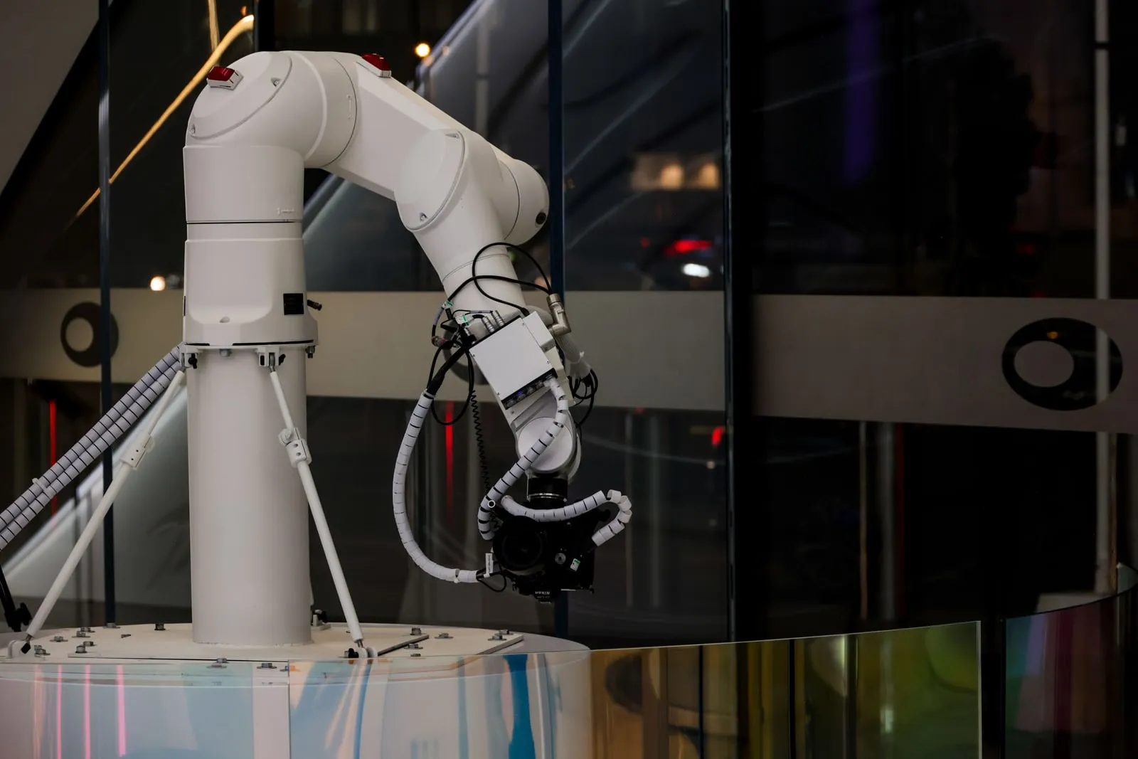 A white robot arm holding a camera behind a glass panel