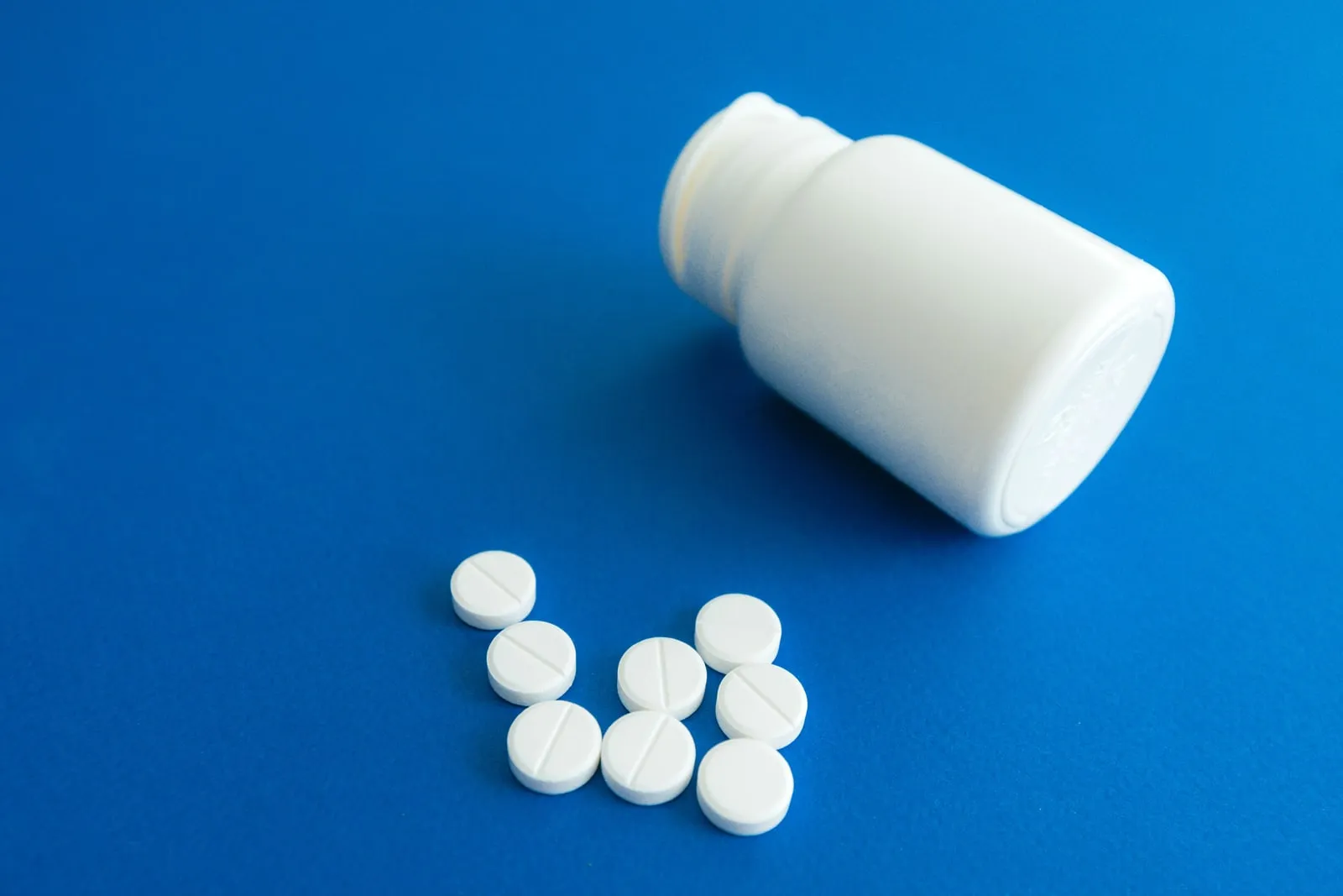 White pills spilled from a bottle onto a plain blue surface