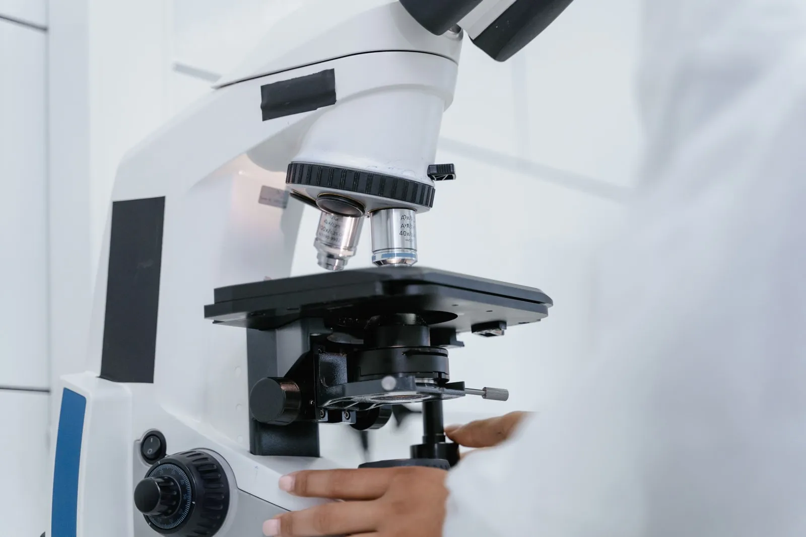 Um microscópio de laboratório com a mão de uma investigadora no botão de focagem