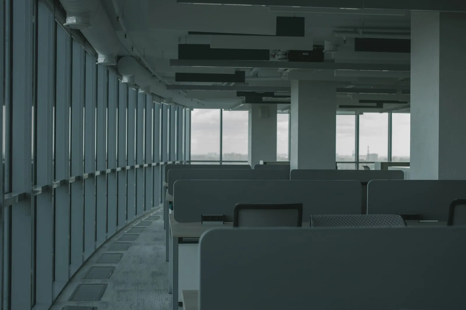 Rows of empty desks beside a window wall in a large office