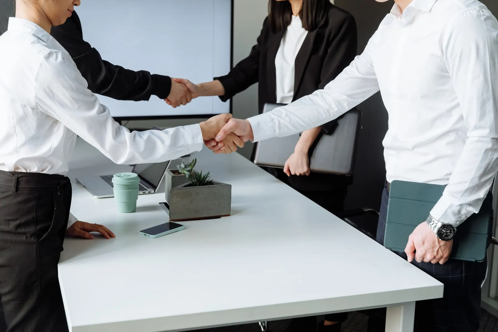 Two people shaking hands across a conference table