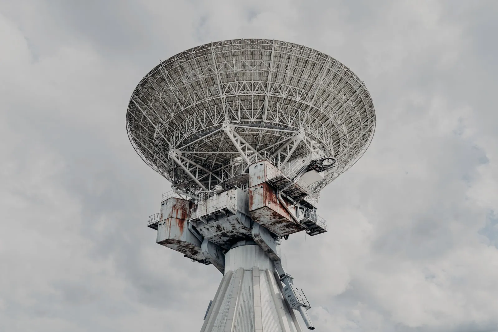 A large radar antenna dish seen from below against an overcast sky